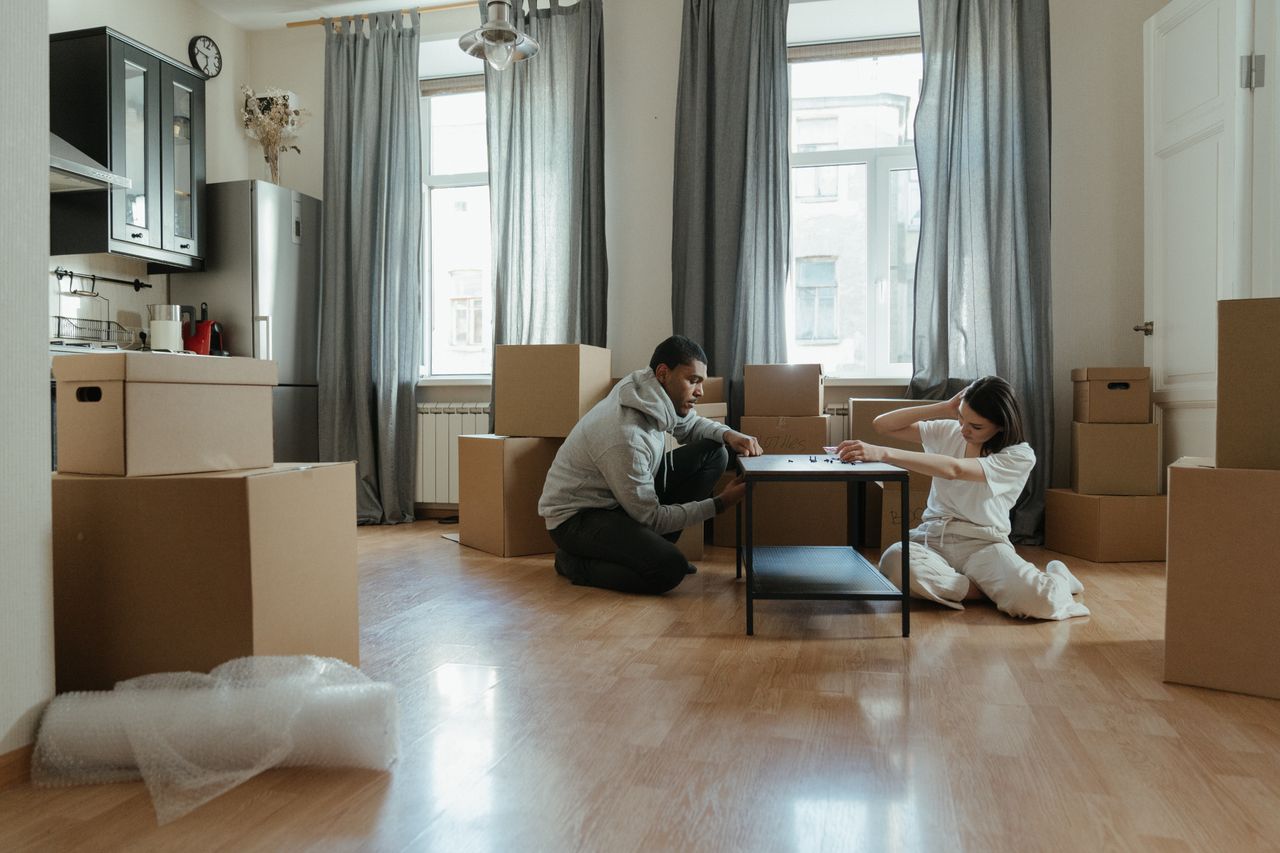 Young couple putting together furniture in their new apartment, surrounded by cardboard boxes.